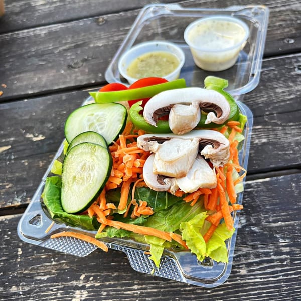 Fresh garden salad with lettuce, cucumbers, carrots, mushrooms, and bell peppers, with two dressings.