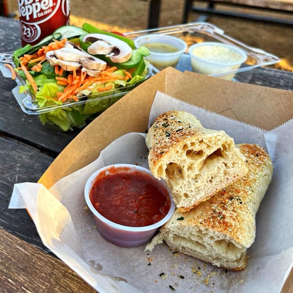 Garlic knots with marinara, a side salad, and a Dr. Pepper on a wooden table.