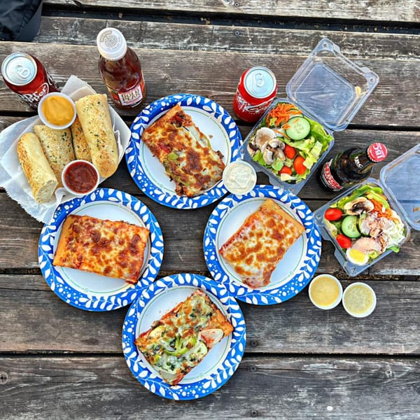 An overhead view of pizza slices, garlic bread, salads, and drinks on a rustic wooden table.