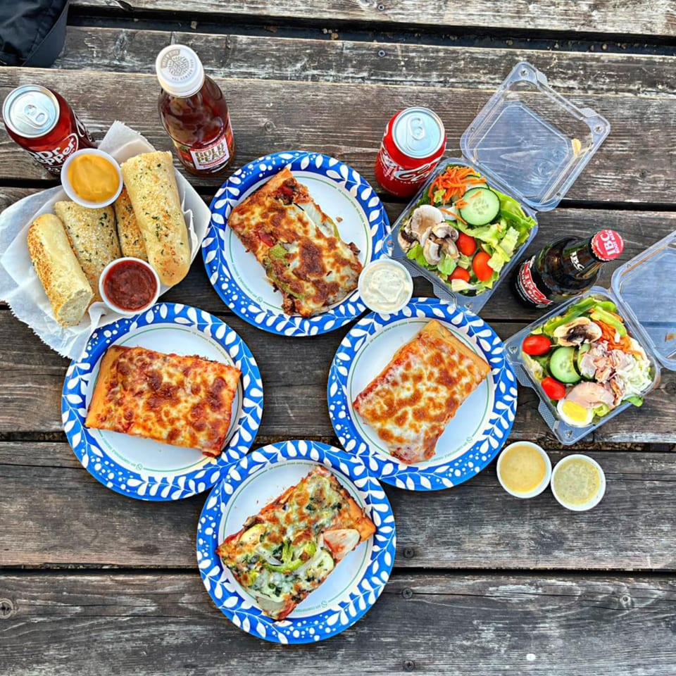 An overhead view of pizza slices, garlic bread, salads, and drinks on a rustic wooden table.