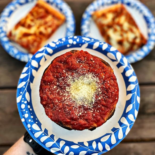 A deep-dish pizza with rich tomato sauce and parmesan, with two pizza slices in the background.